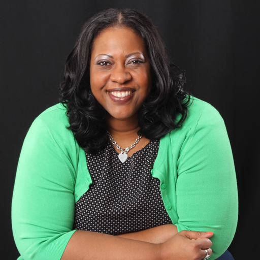 A photo of Aprill O. Turner, a Black woman with shoulder length loose curls, a silver necklace, a black and white polka dot blouse and a mint green cardigan.