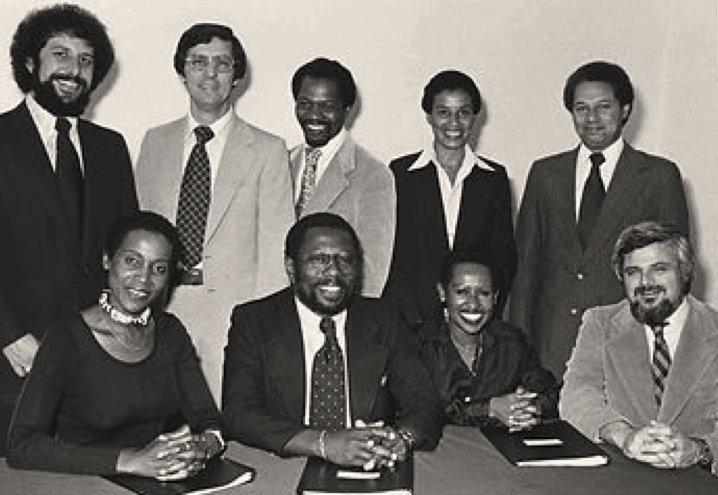 A black and white photo of people in professional dress, late 1970s. The founders of the Maynard Institute. Top row, from left: Steve Montiel, Frank Sotomayor, Earl Caldwell, Nancy Hicks Maynard, John Dotson. Bottom Row, from left: Dorothy Butler Gilliam, Robert C. Maynard, an unknown person, and LeRoy 