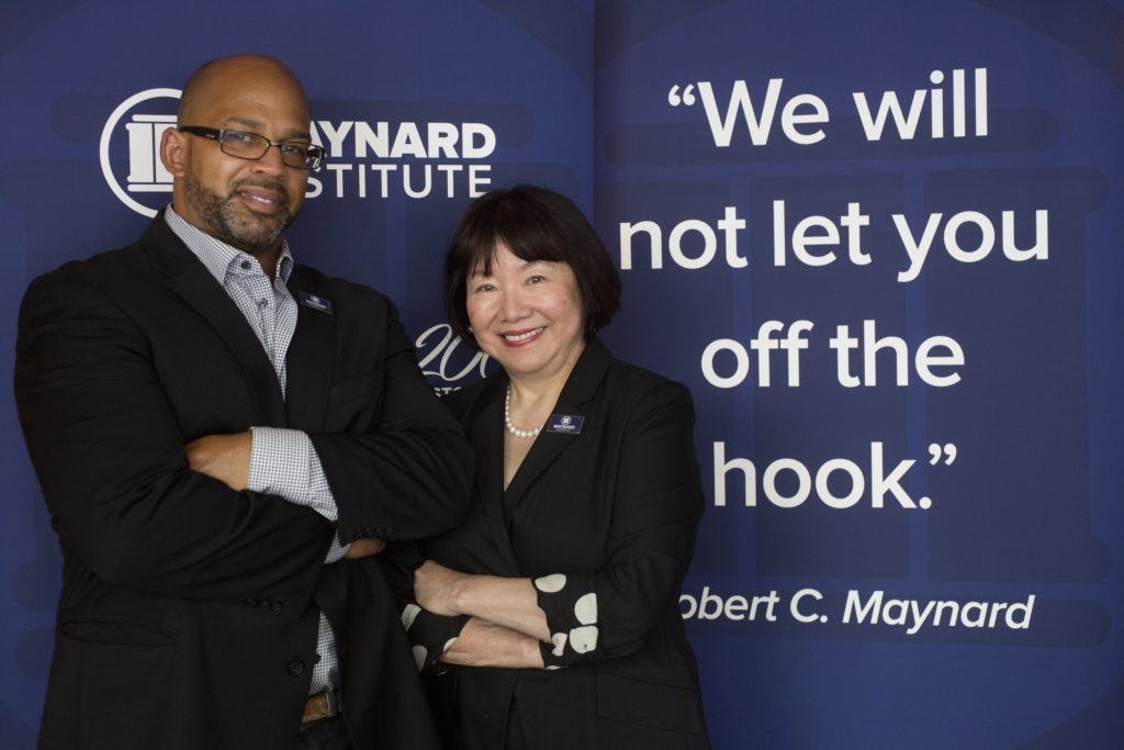 A photo of Martin G. Reynolds, a Black man, bald and wearing glasses and professional attire, standing before a dark blue banner with Maynard Institute branding. Next to him, Evelyn Hsu, an older Asian woman with a bob haircut and bangs wearing a black suit pearls. Beside her, part of the banner reads "We will not let you off the hook." Robert C. Maynard.