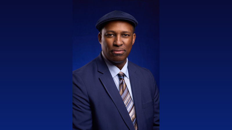 A photograph of William J. Ford, a Black m a wearing a dark blue suit and tie, along with dark blue flat-cap hat.